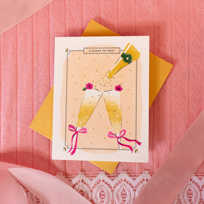 peach card with two gold champagne glasses